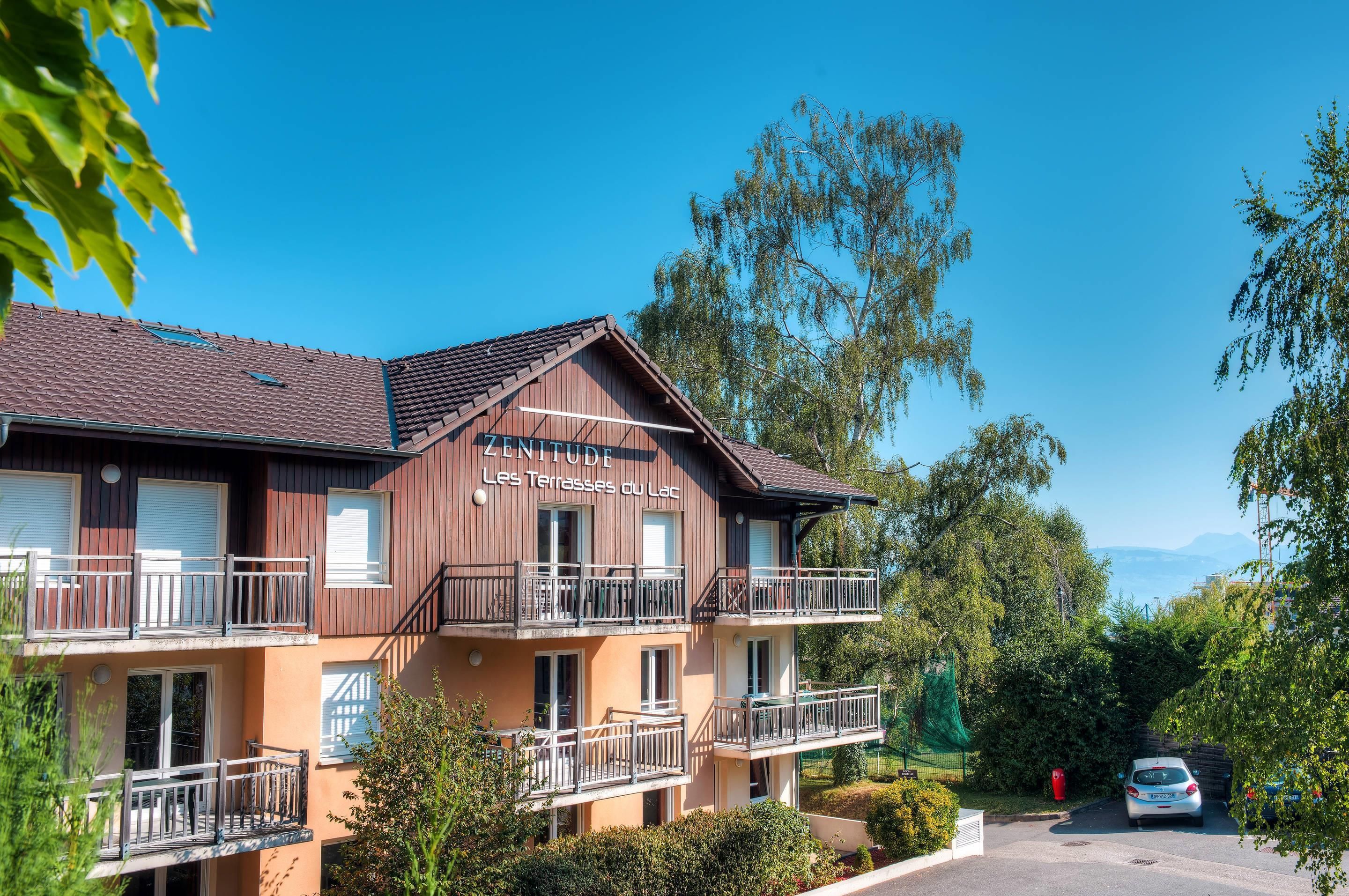 A two-story hotel with balconies and a clear view of the surrounding greenery and mountains.