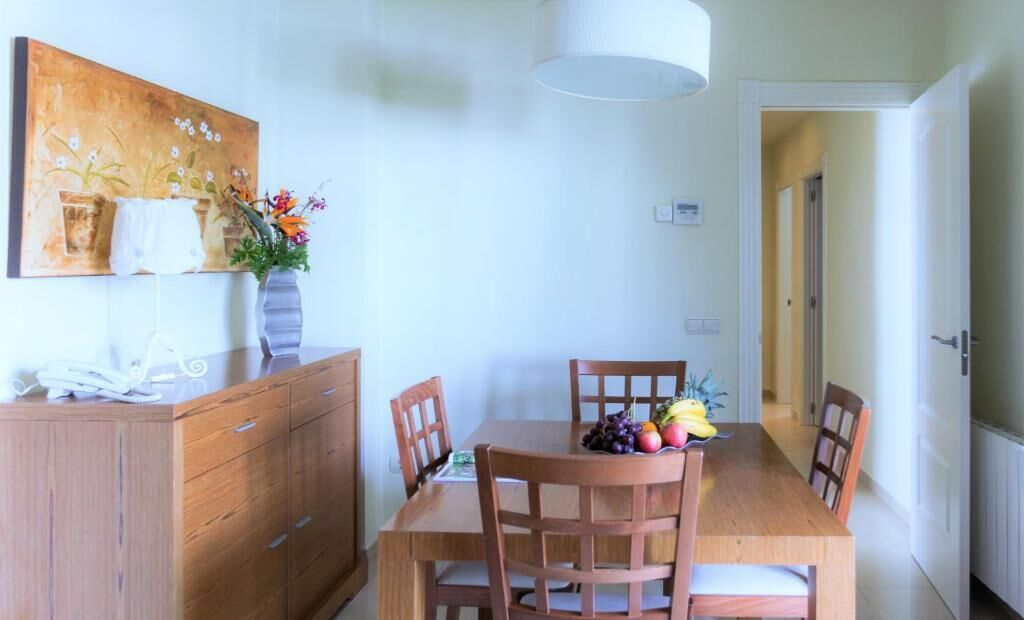 Un coin repas avec une table et des chaises en bois, un vase rempli de fleurs et un tableau accroché au mur.