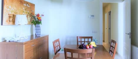 A dining area with a wooden table and chairs, a vase with flowers, and a painting on the wall.