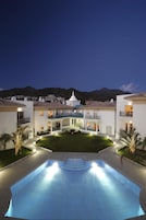 A hotel with a swimming pool, multiple balconies, and a view of mountains.