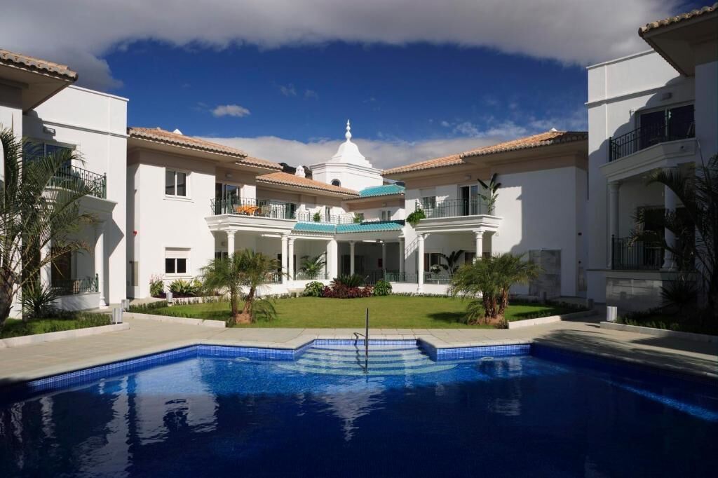 A large, white building with a central dome and multiple balconies, surrounded by a swimming pool.