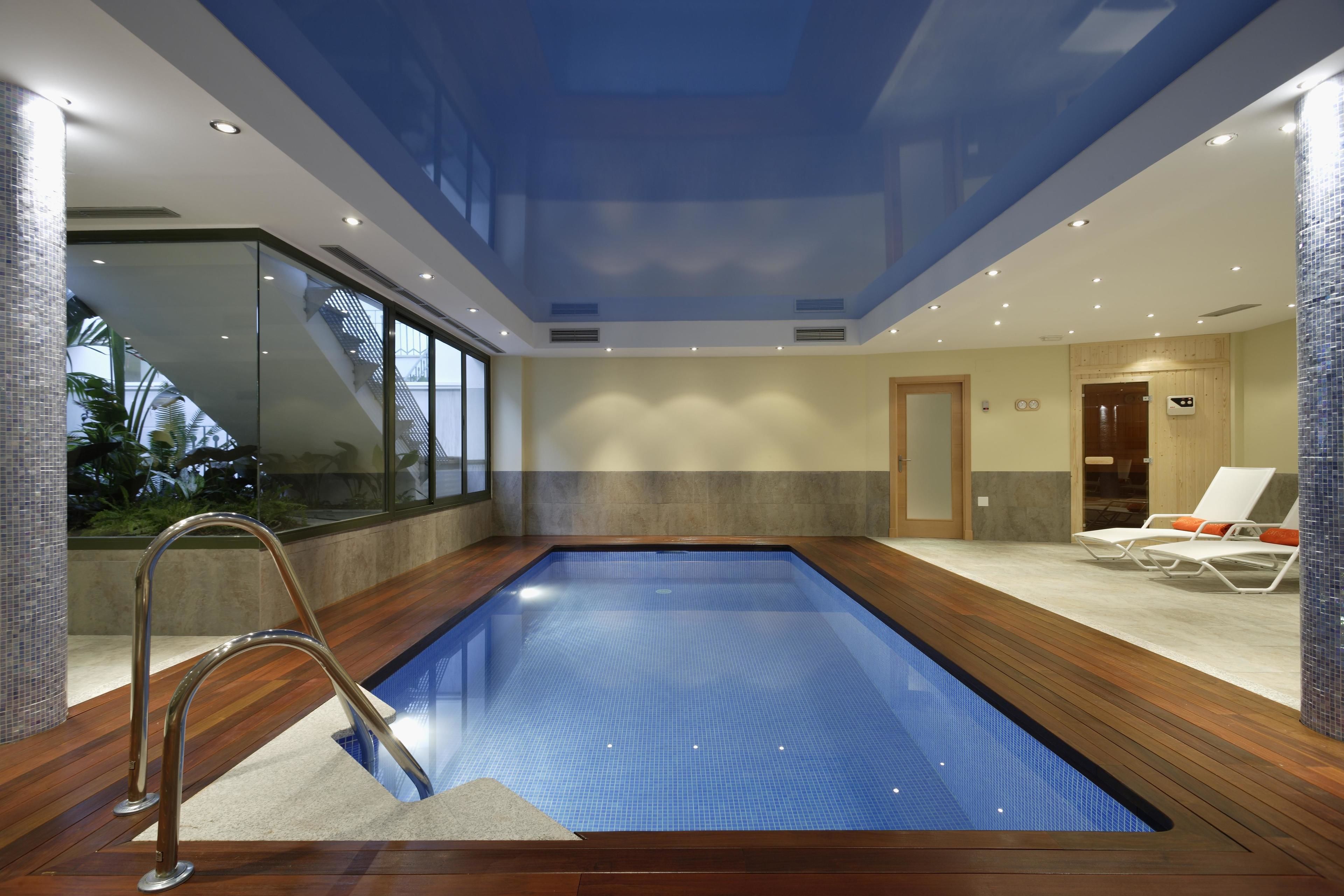 Une piscine intérieure dotée d’une paroi en verre, d’une terrasse en bois et de chaises longues.