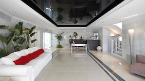 Ein modernes Interieur mit einem weißen Sofa, roten Kissen, einem Essbereich und einer Treppe.