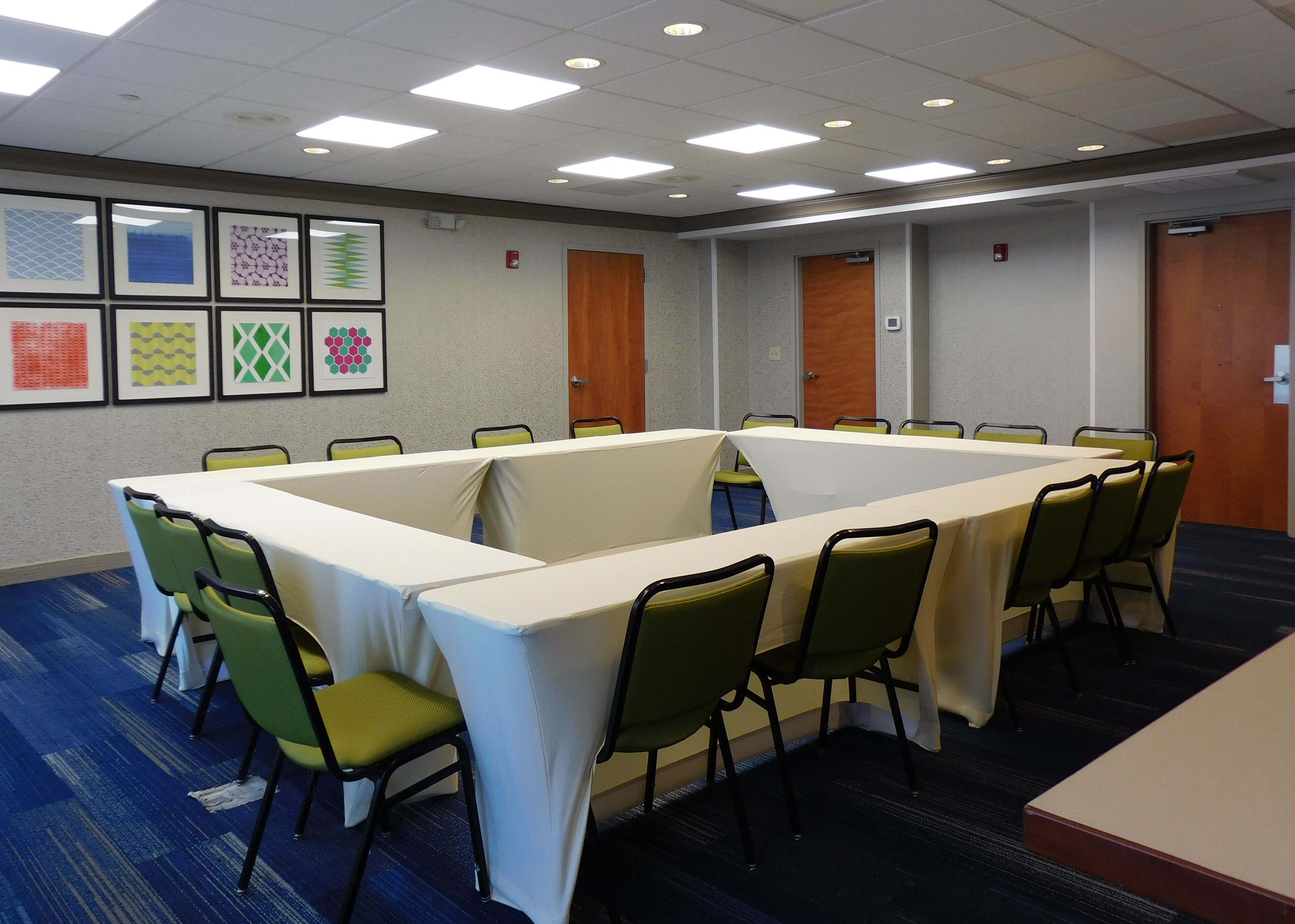 A conference room with a long table and chairs, framed artwork on the walls, and doors in the background.