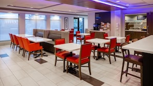 Un restaurant moderne avec des chaises rouges et des tables blanches, un coin bar et de grandes fenêtres.