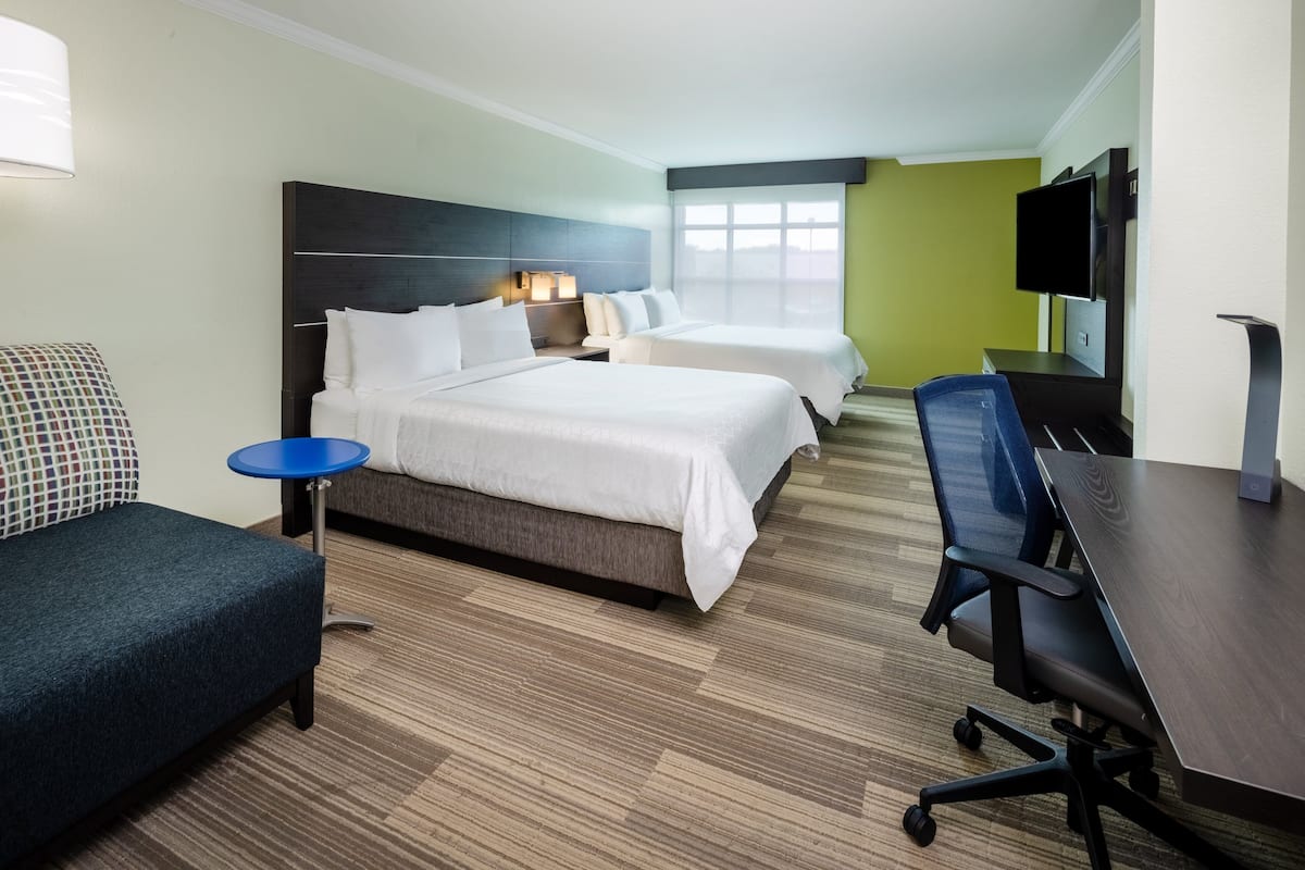 A hotel room with two beds, a desk, a chair, a TV, and a window.