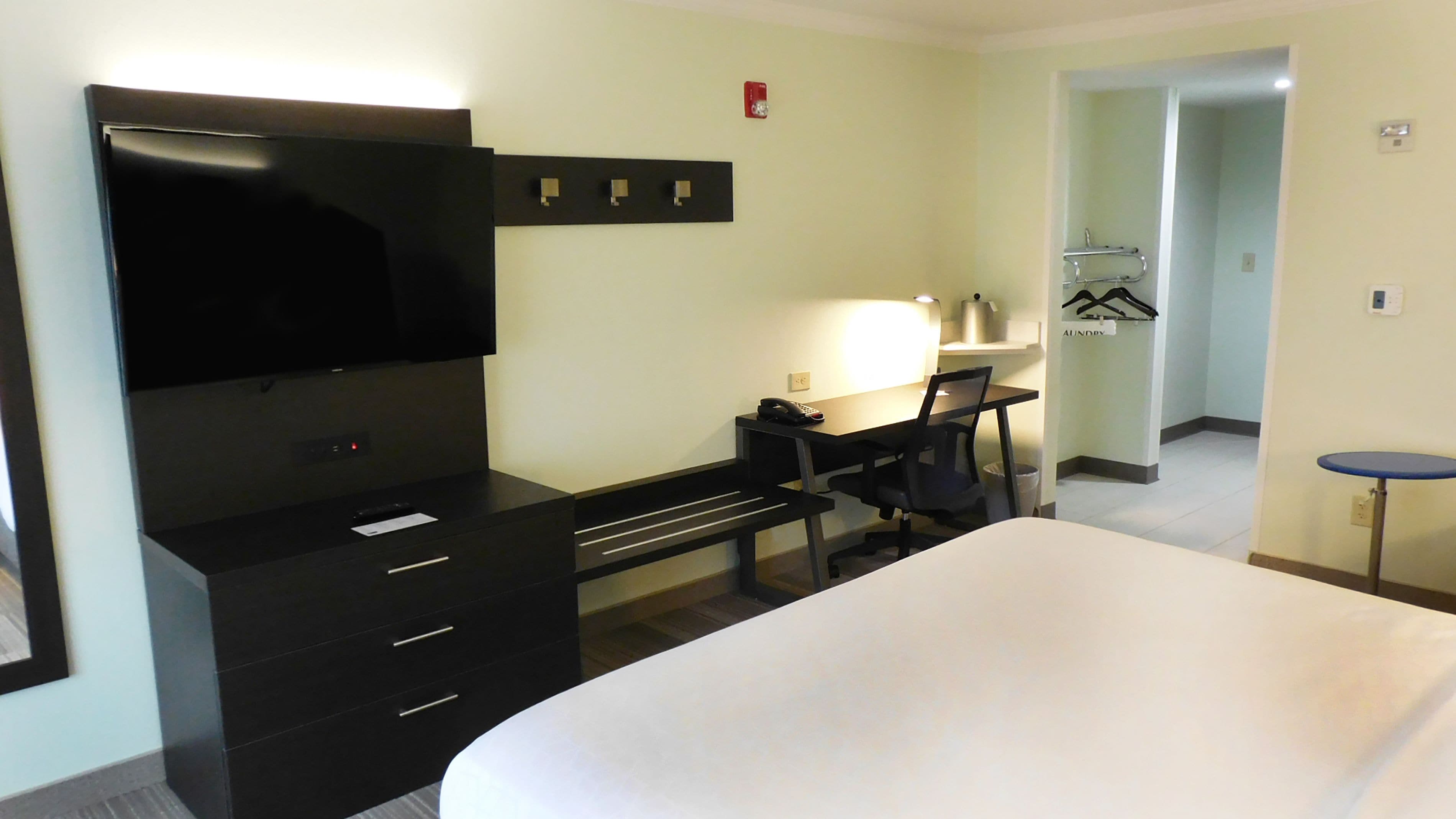 A hotel room with a bed, a desk with a chair, a TV, a lamp, and a small table.