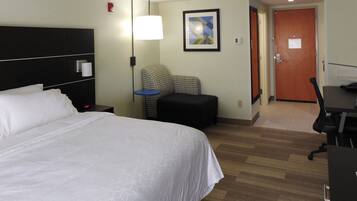 A hotel room with a large bed, a desk, a chair, a lamp, and a door.