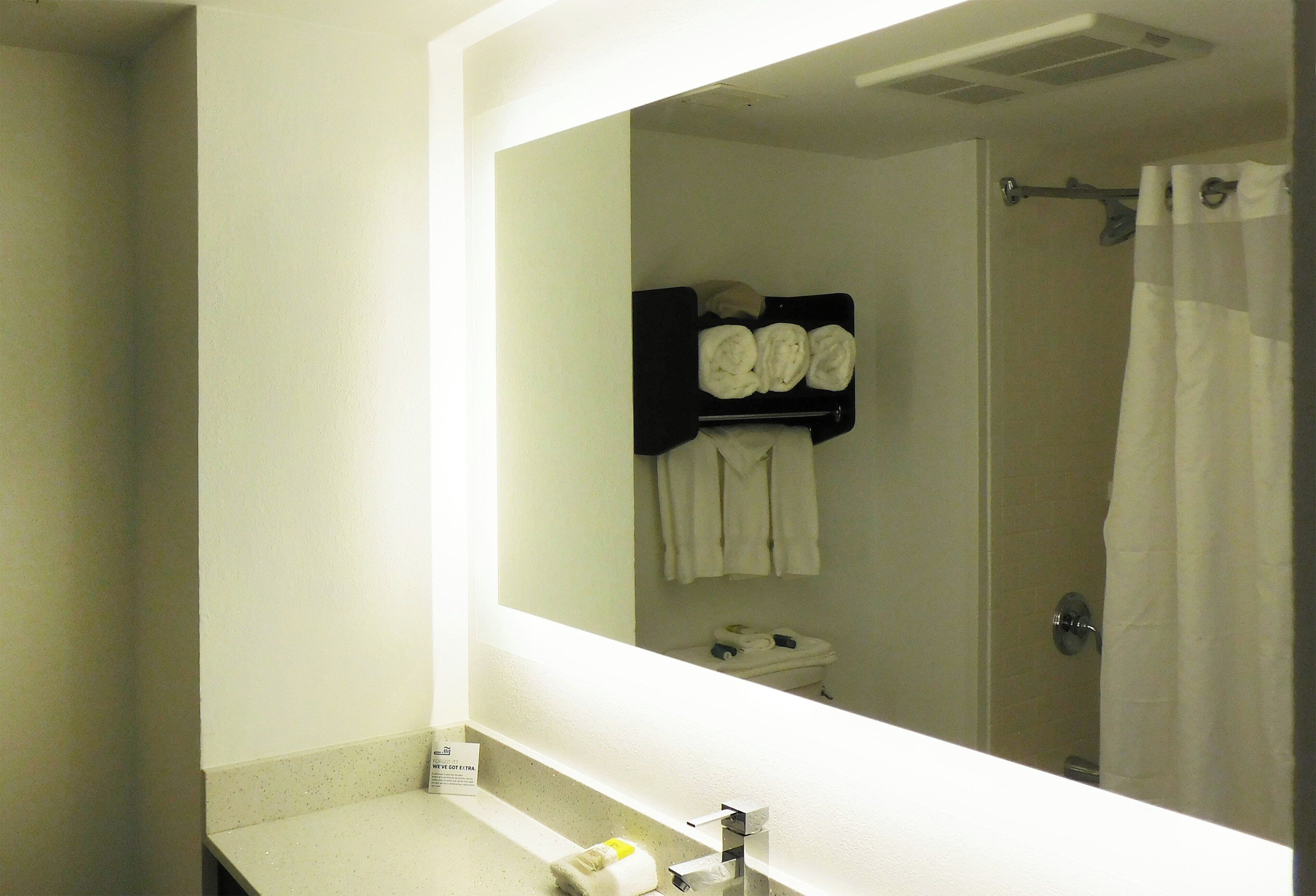 A bathroom with a large mirror, a sink, and a towel rack with towels.