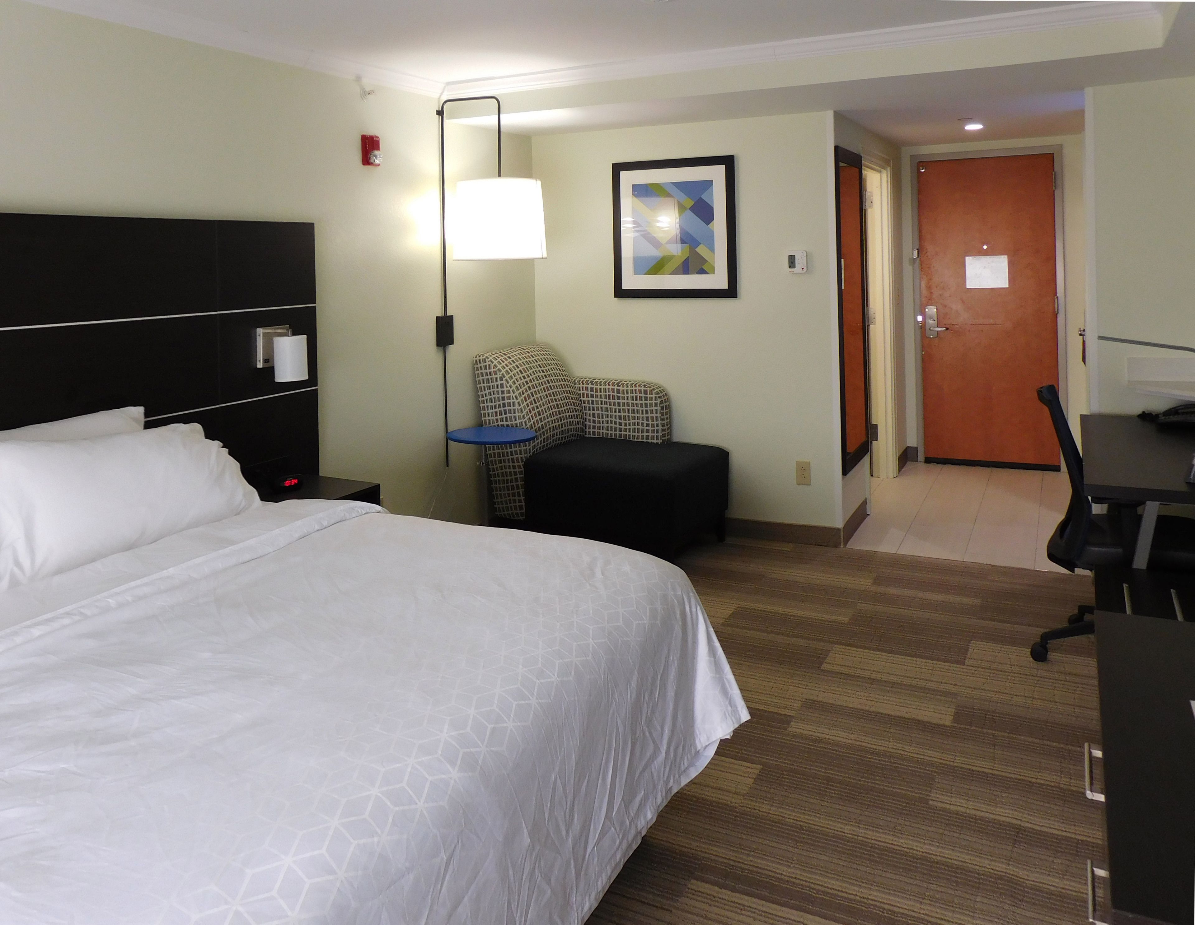 Una habitación de hotel con una cama grande, un escritorio, una silla, una lámpara y una puerta.