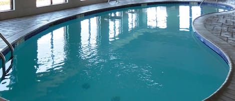 An indoor swimming pool with clear water, surrounded by windows and a tiled deck.