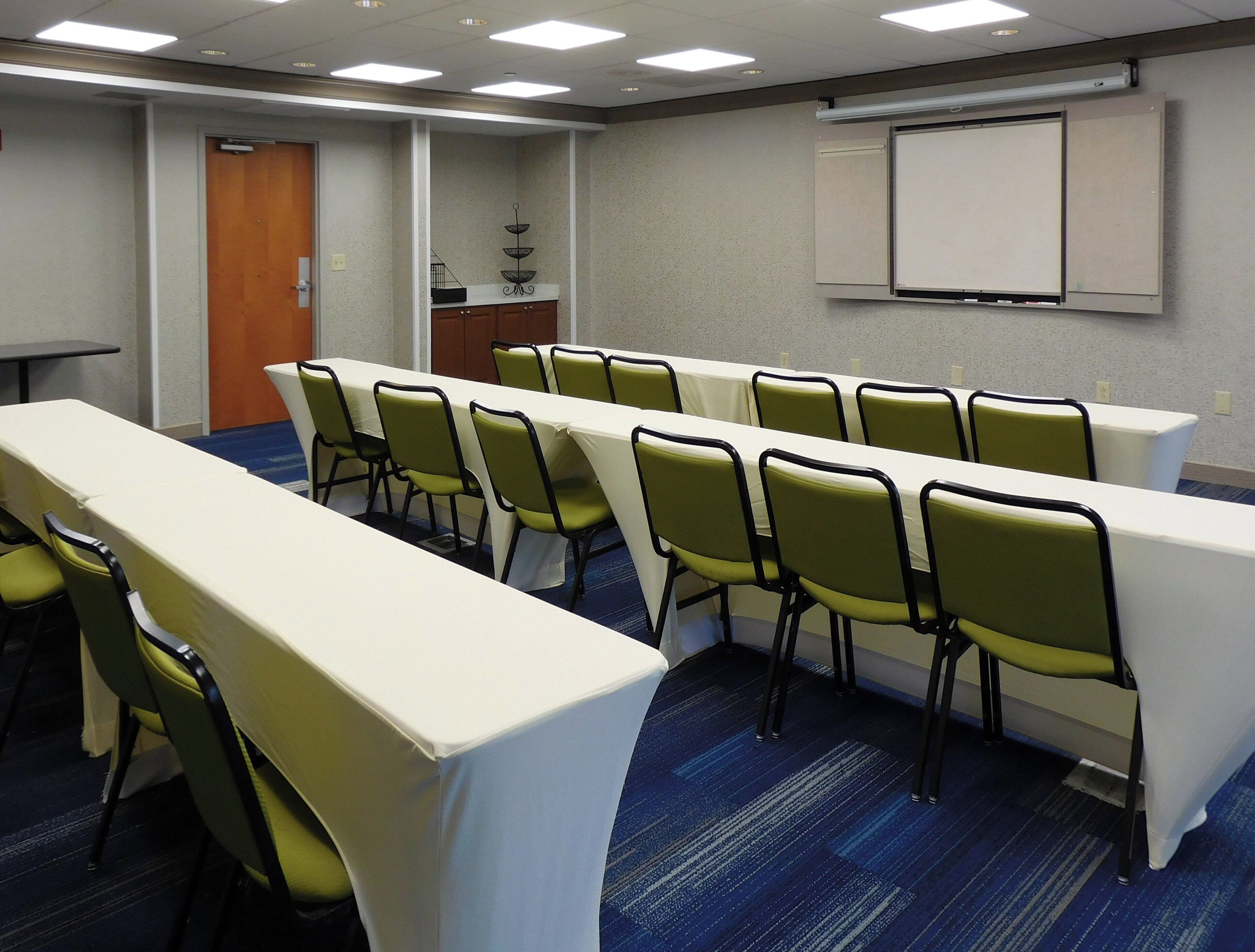 A conference room with a long table, chairs, a projector screen, and a door.
