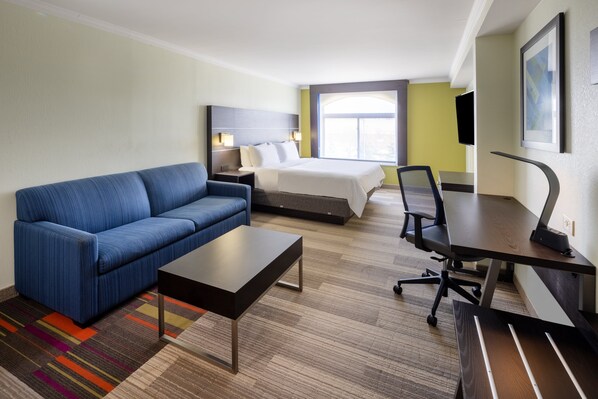 Una habitación de hotel con un sofá azul, una cama, un escritorio y un televisor.