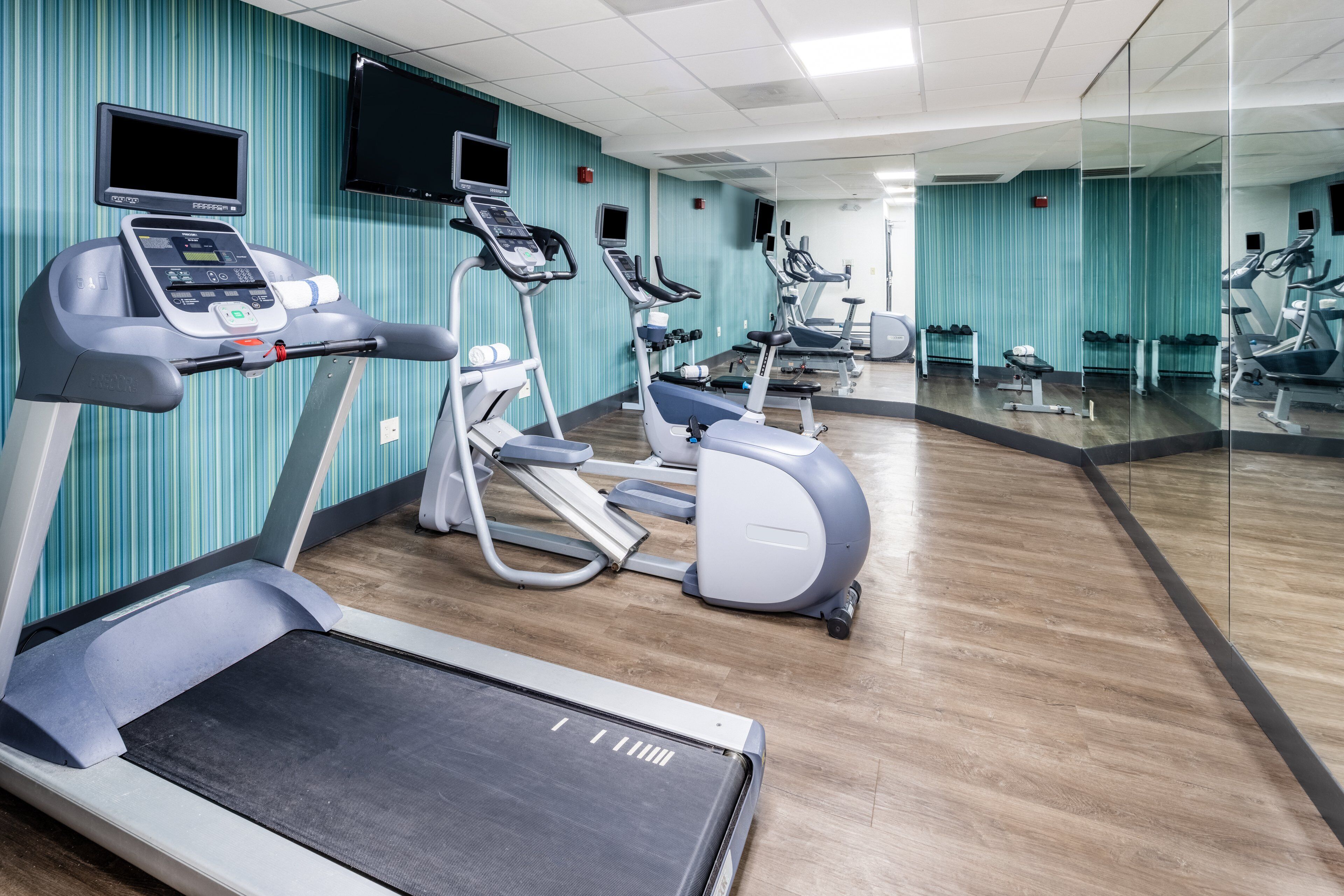A gym with treadmills, ellipticals, and a mirrored wall.