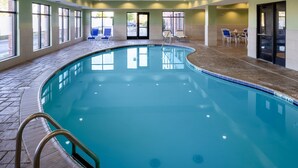 Une piscine intérieure à l’eau d’un bleu limpide, entourée d’un sol carrelé et de grandes fenêtres.