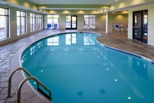 Una piscina interior con agua azul cristalina, rodeada de suelo de baldosas y grandes ventanales.