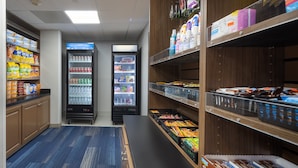 Une  épicerie dont les étagères sont remplies d’en-cas et de boissons, avec deux réfrigérateurs et un comptoir où sont exposés des produits emballés.