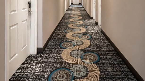 A hotel hallway with a patterned carpet, white walls, and a red emergency light. - Super 8 by Wyndham Lake Country/Winfield Area Airport North (Lake Country)