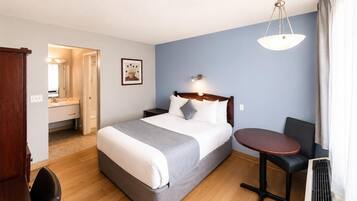 Quarto de hotel com cama, mesa de cabeceira, cadeira, escrivaninha e aparelho de ar condicionado.