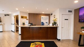 A hotel reception area with a reception desk, a 'Free Park & Fly' sign, a 'Super 8 by Wyndham' carpet, a staircase, and a 'Employees Only' door. - Super 8 by Wyndham Lake Country/Winfield Area Airport North (Lake Country)