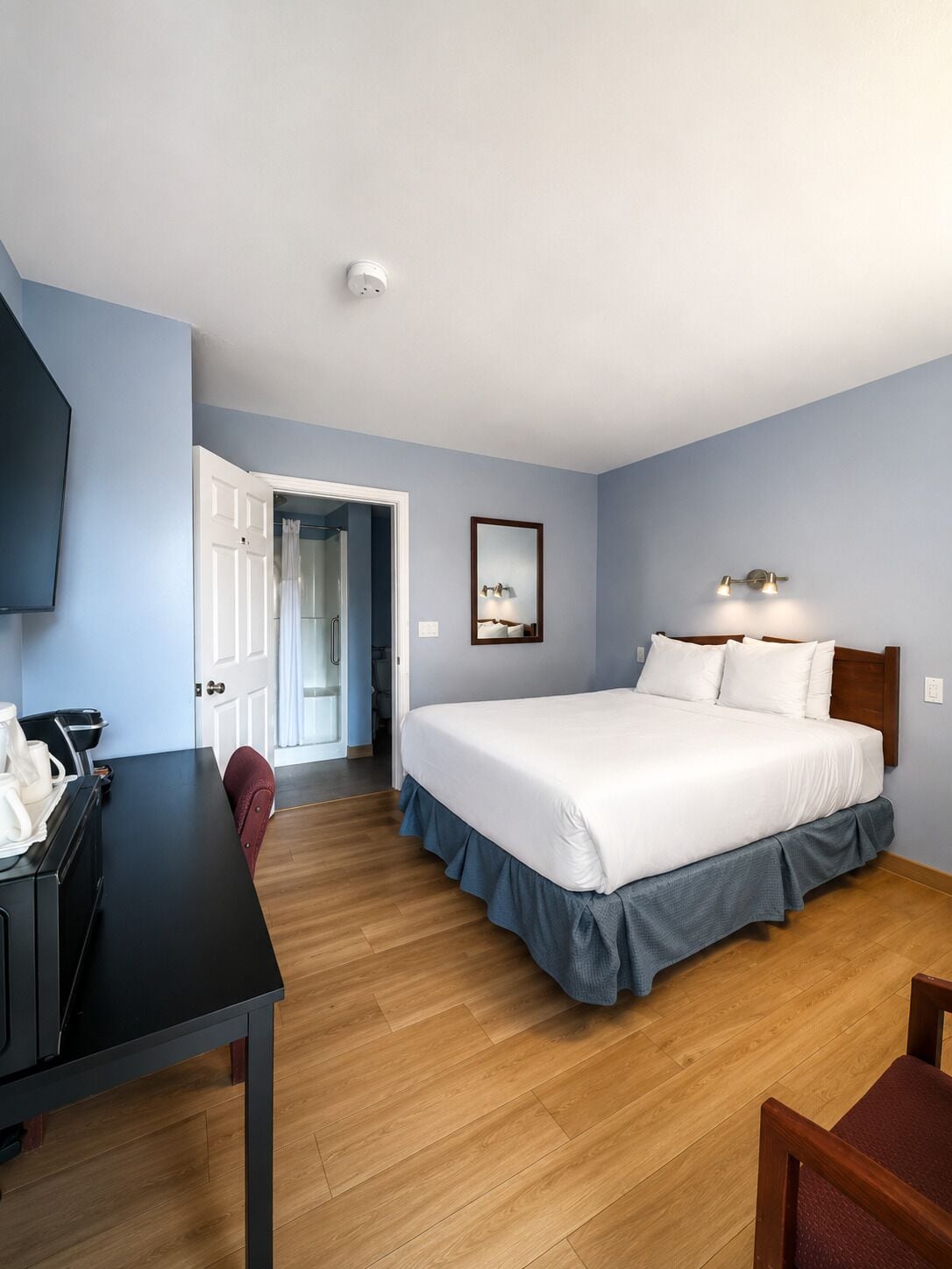 Une chambre d’hôtel équipée d’un lit, d’un bureau, d’une chaise, d’une télévision et d’une porte donnant accès à une salle de bain.