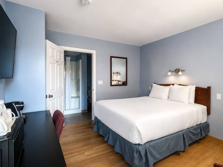 Une chambre d’hôtel équipée d’un lit, d’un bureau, d’une chaise, d’une télévision et d’une porte donnant accès à une salle de bain.