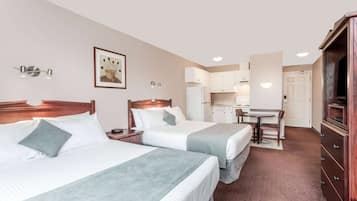 Ein Hotelzimmer mit zwei Betten, einem Schreibtisch, einer Küchenzeile und einem Fernseher.
