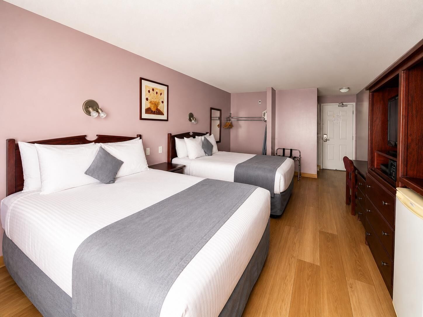 A hotel room with two beds, a wooden dresser, a television, and a door leading to another room.