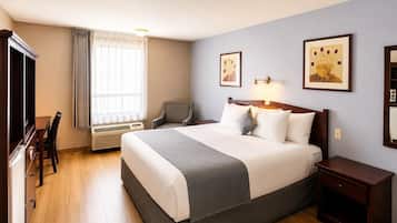 Habitación de hotel con cama, mesita de noche, silla, escritorio y un ventanal con cortinas.