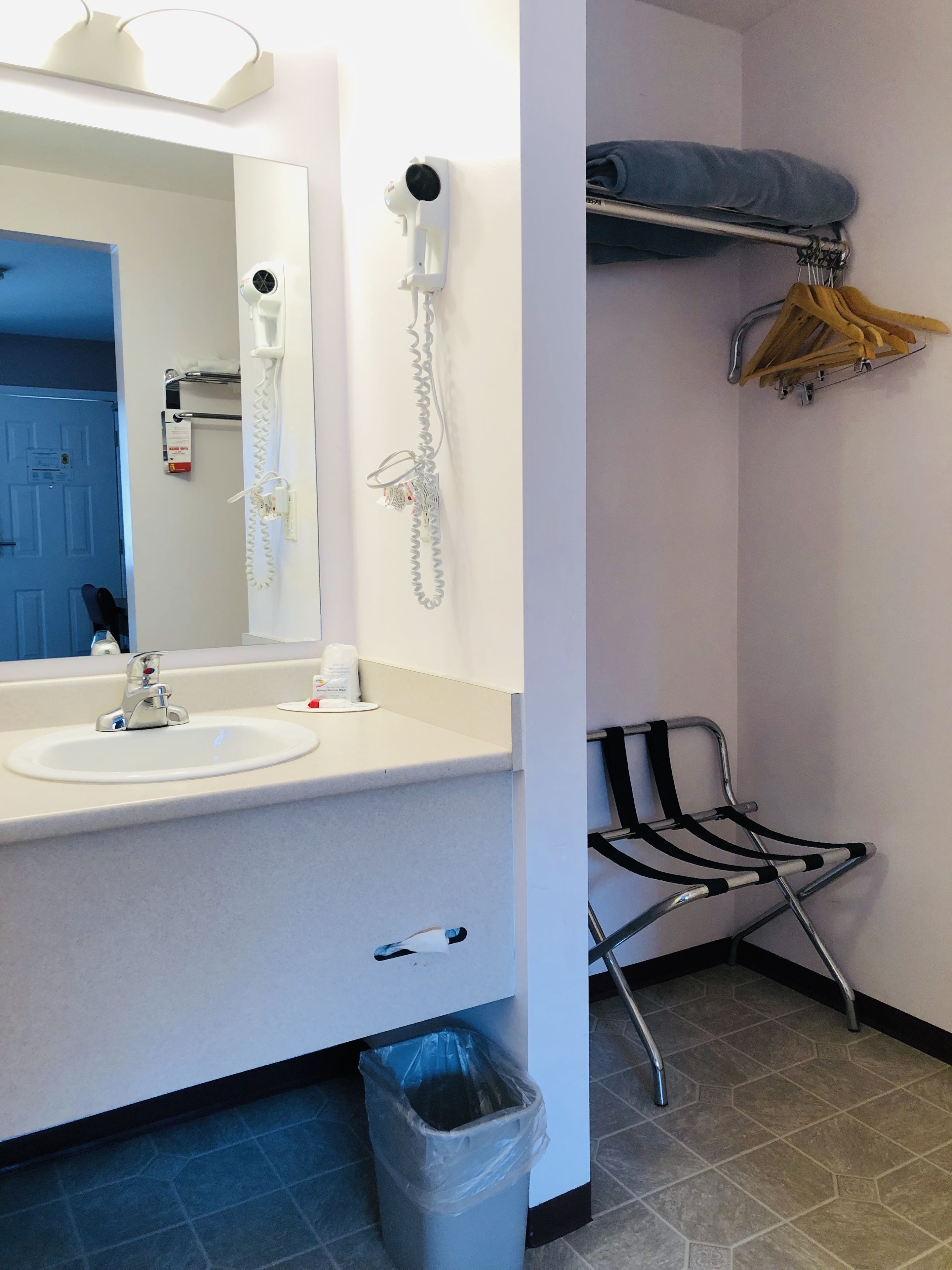 Un baño con lavamanos, espejo, secador de pelo y toallero.