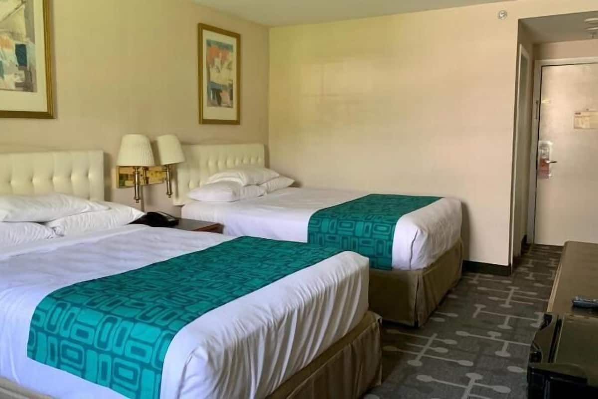 Una habitación de hotel con dos camas, cabecera, lámpara y puerta.