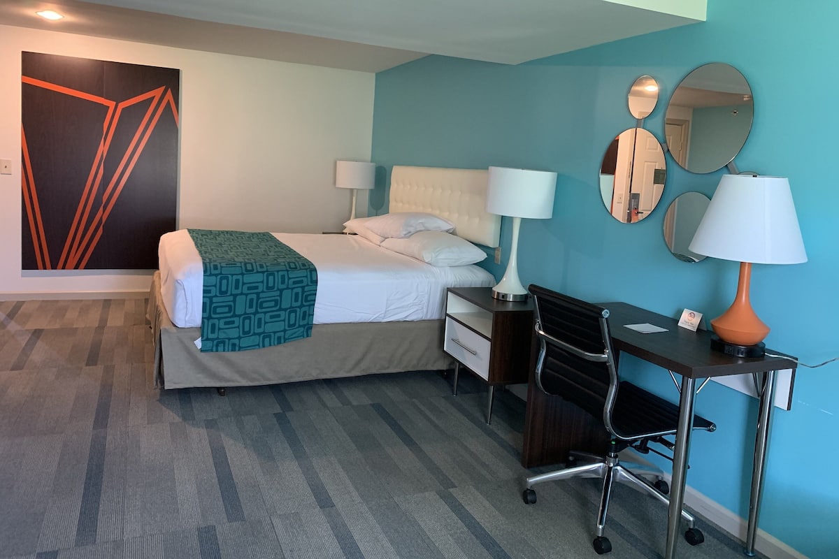 Una habitación de hotel con cama, escritorio, silla y dos lámparas.