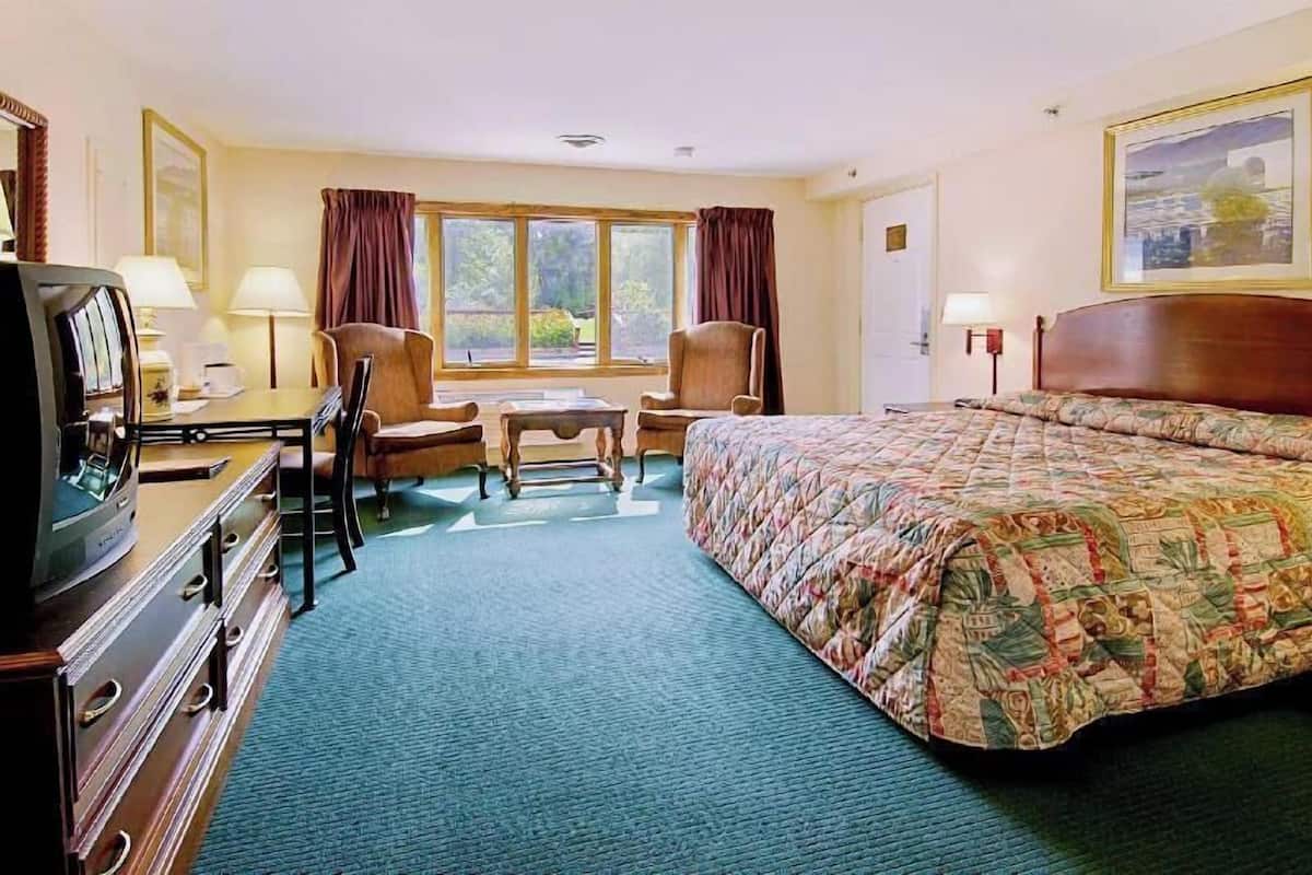 Habitación de hotel con cama, escritorio con televisor, dos sillas, una mesa y ventana con cortinas.