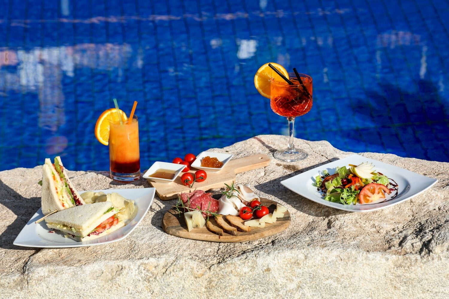 A poolside dining setup with a sandwich, salad, and drinks.