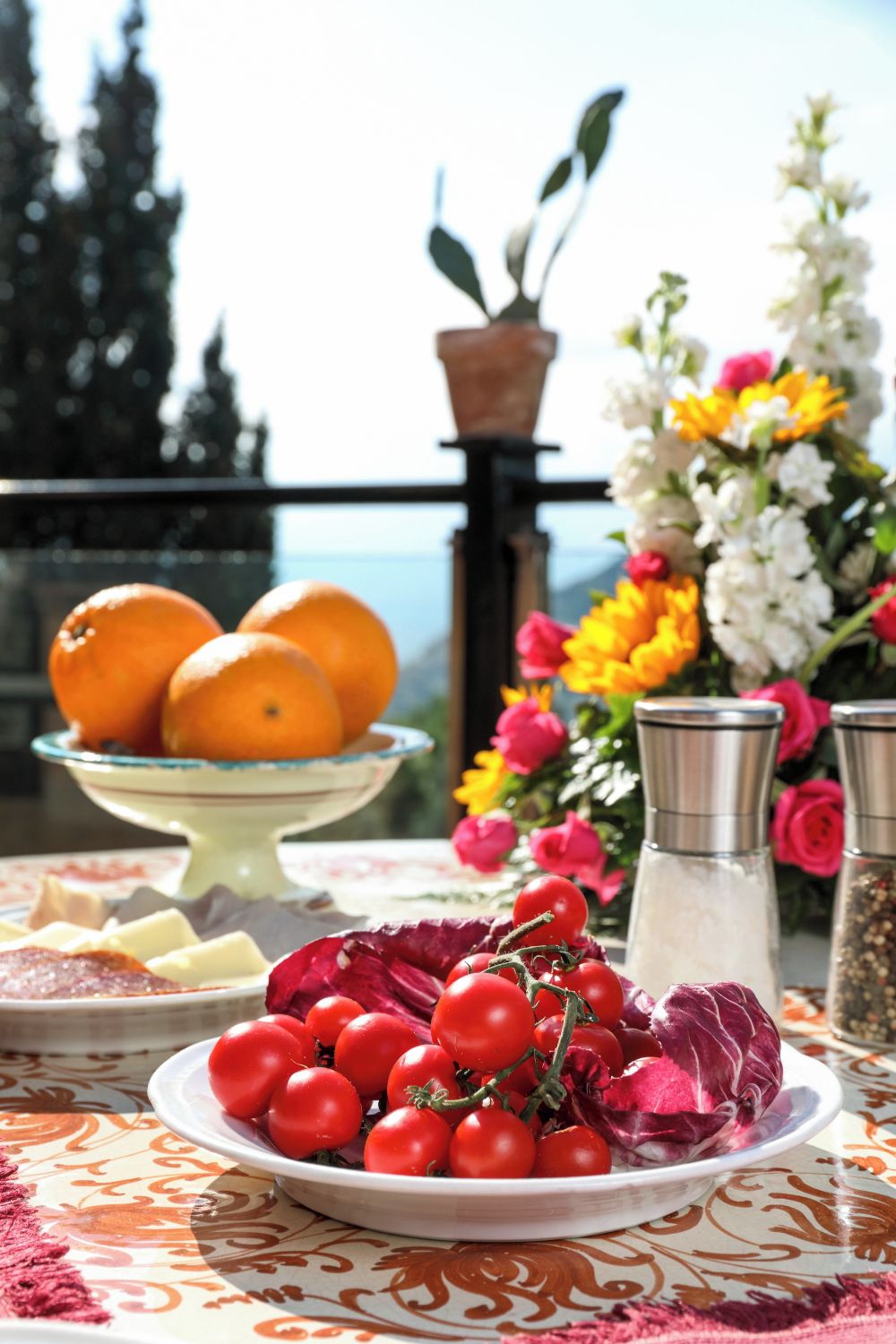 Ein Tisch mit einer Tomatenschale, einer Orangenschüssel und einer dekorativen Vase mit Blumen.