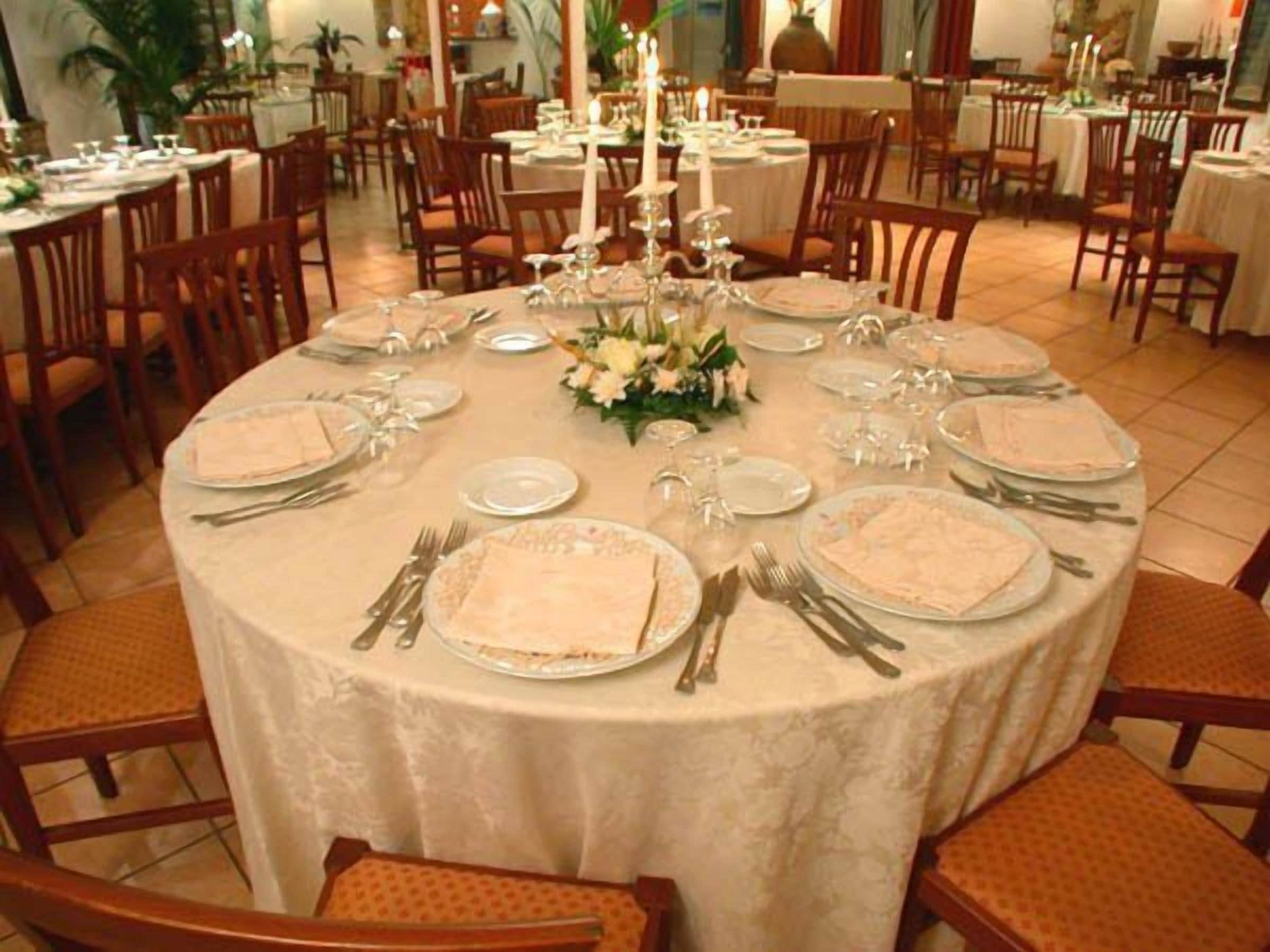 A round dining table set for a formal meal with white tablecloths, silverware, and a centerpiece of flowers.