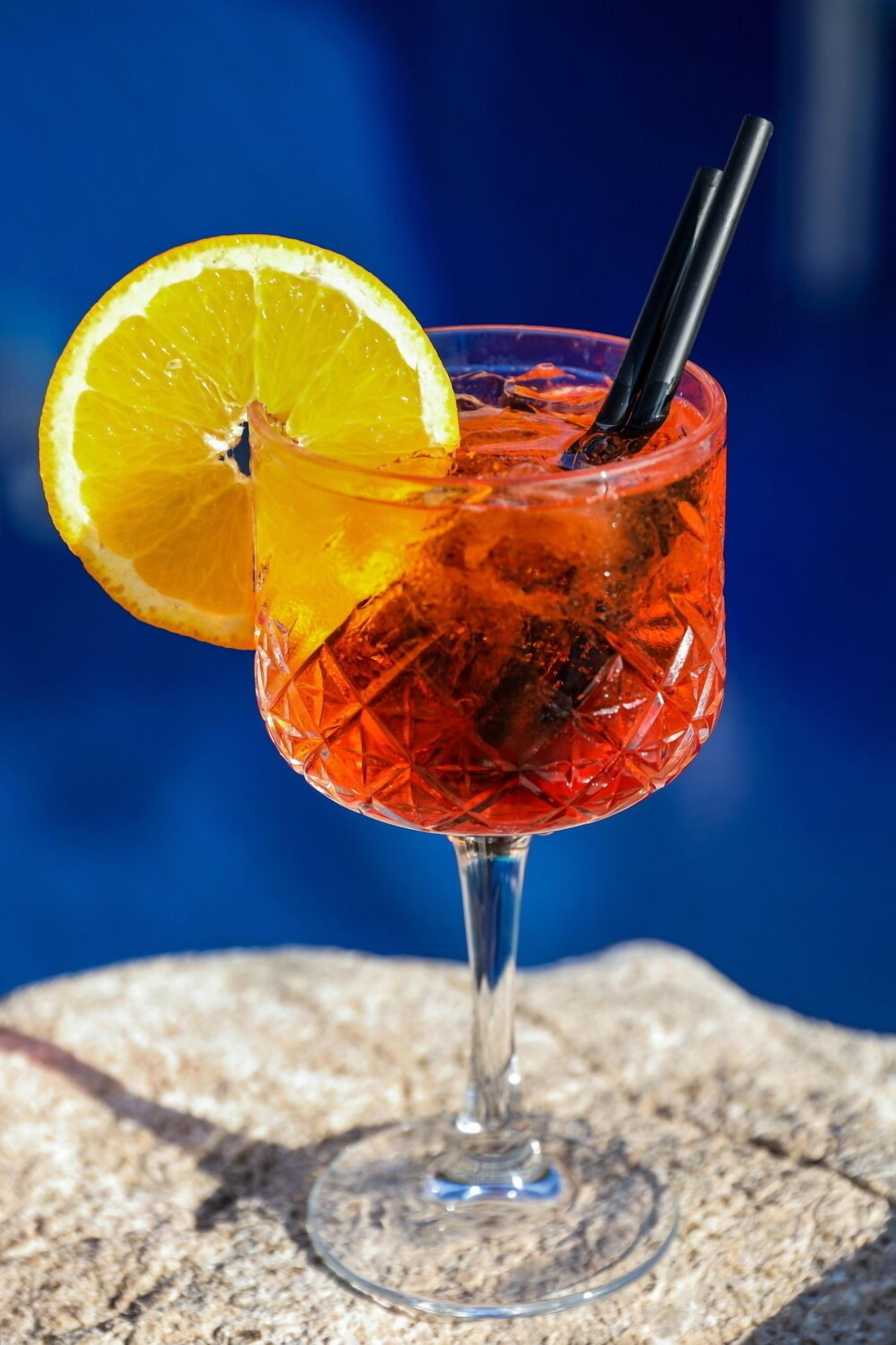 A cocktail in a clear glass with a lemon slice garnish, a straw, and ice cubes.