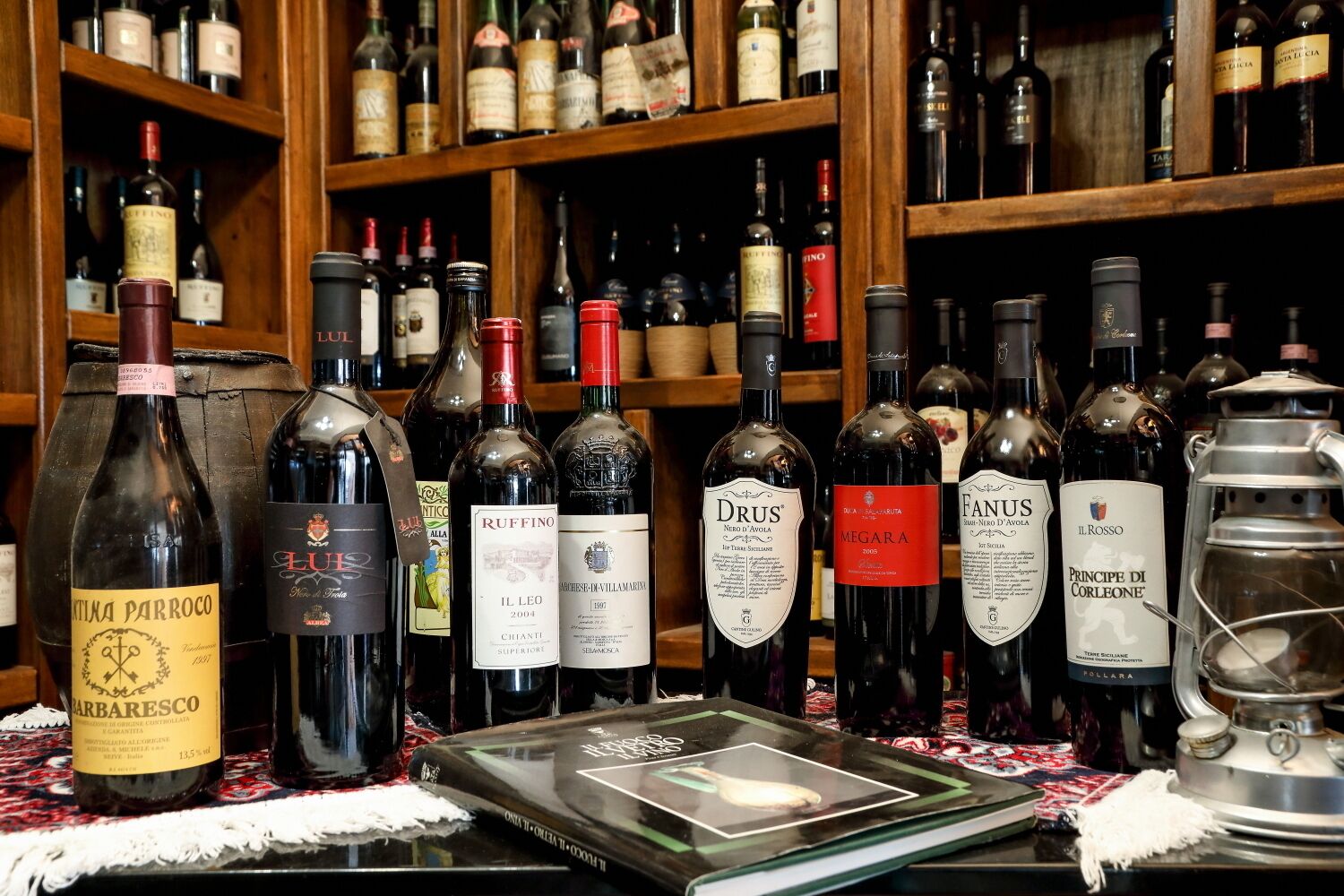 Variedad de botellas de vino expuestas en estanterías y una mesa, con etiquetas que muestran diferentes marcas y tipos.