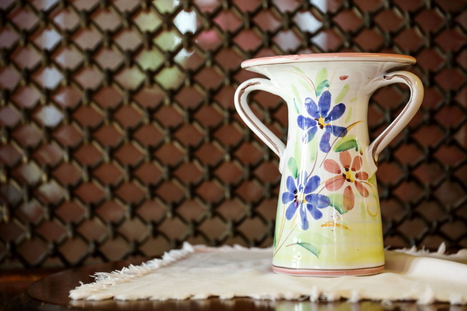 Una jarra de cerámica con diseños florales sobre un mantel.