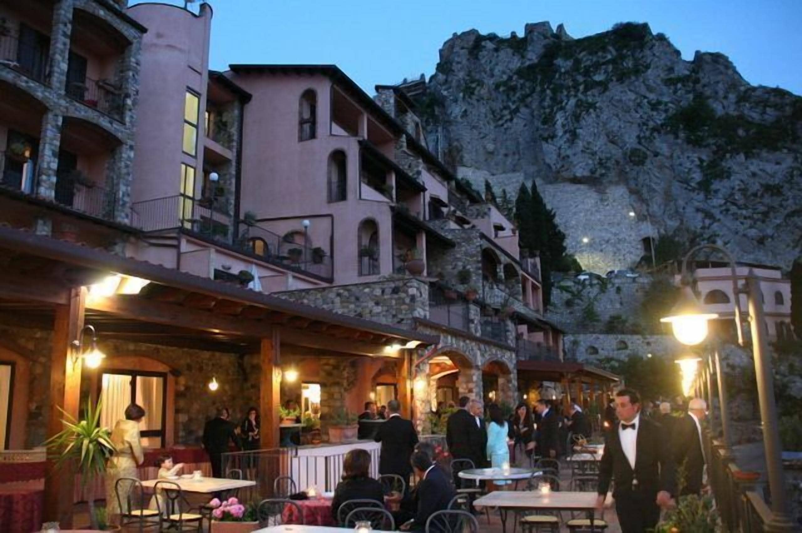 A restaurant with outdoor seating, stone buildings, and a mountainous backdrop.