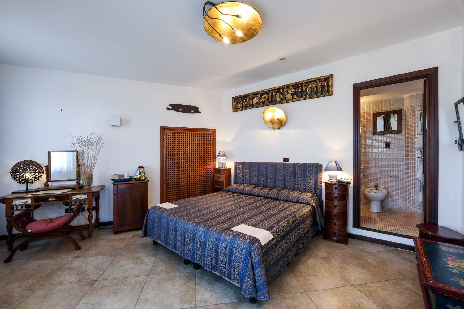 A bedroom with a bed, desk, chair, wardrobe, and a bathroom with a shower and sink.