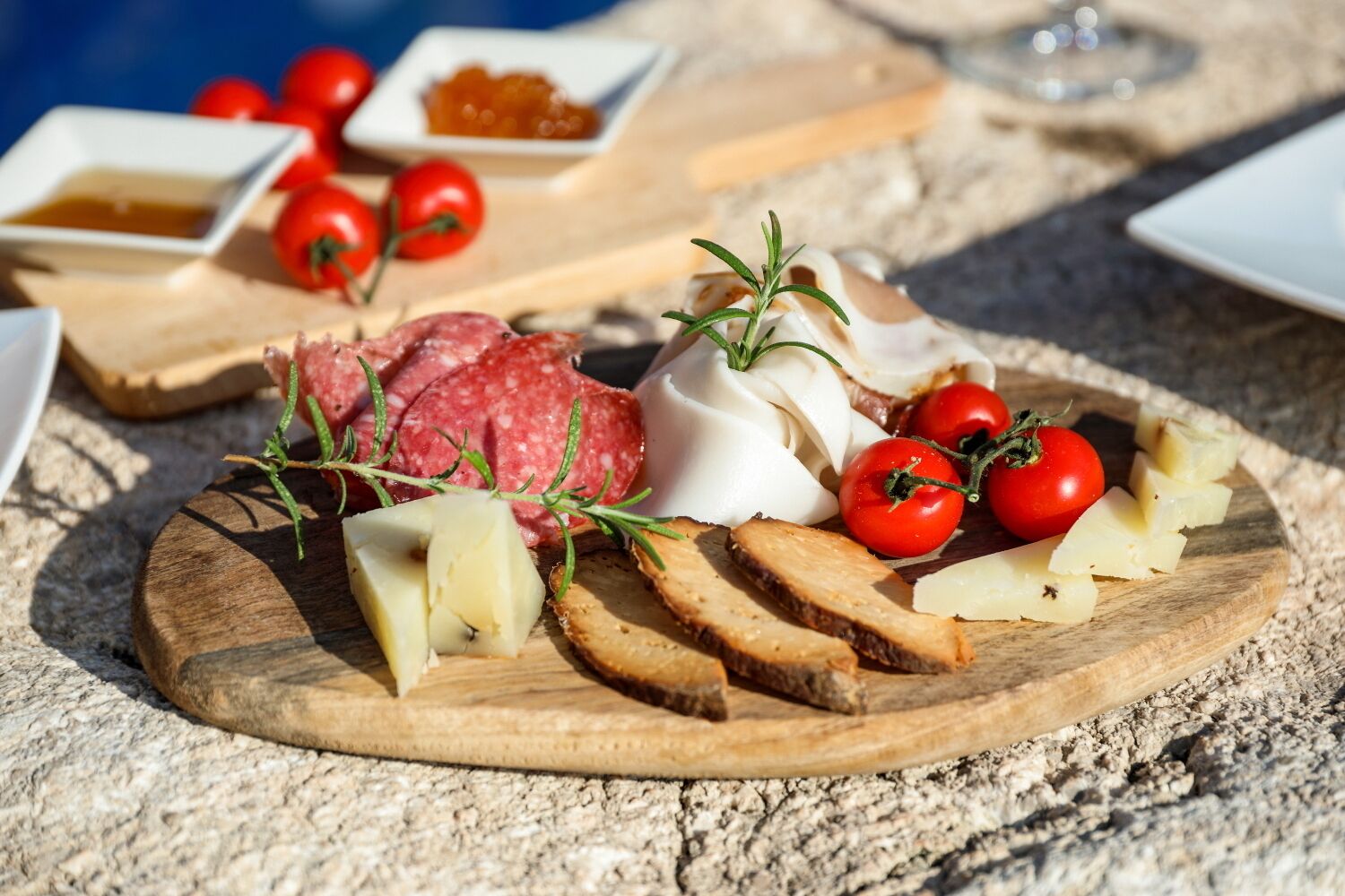 A charcuterie board with various meats, cheeses, and tomatoes on a wooden board.