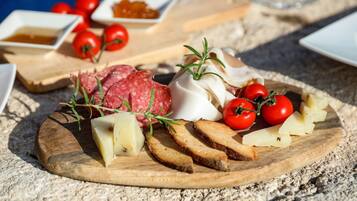 A charcuterie board with various meats, cheeses, and tomatoes on a wooden board.