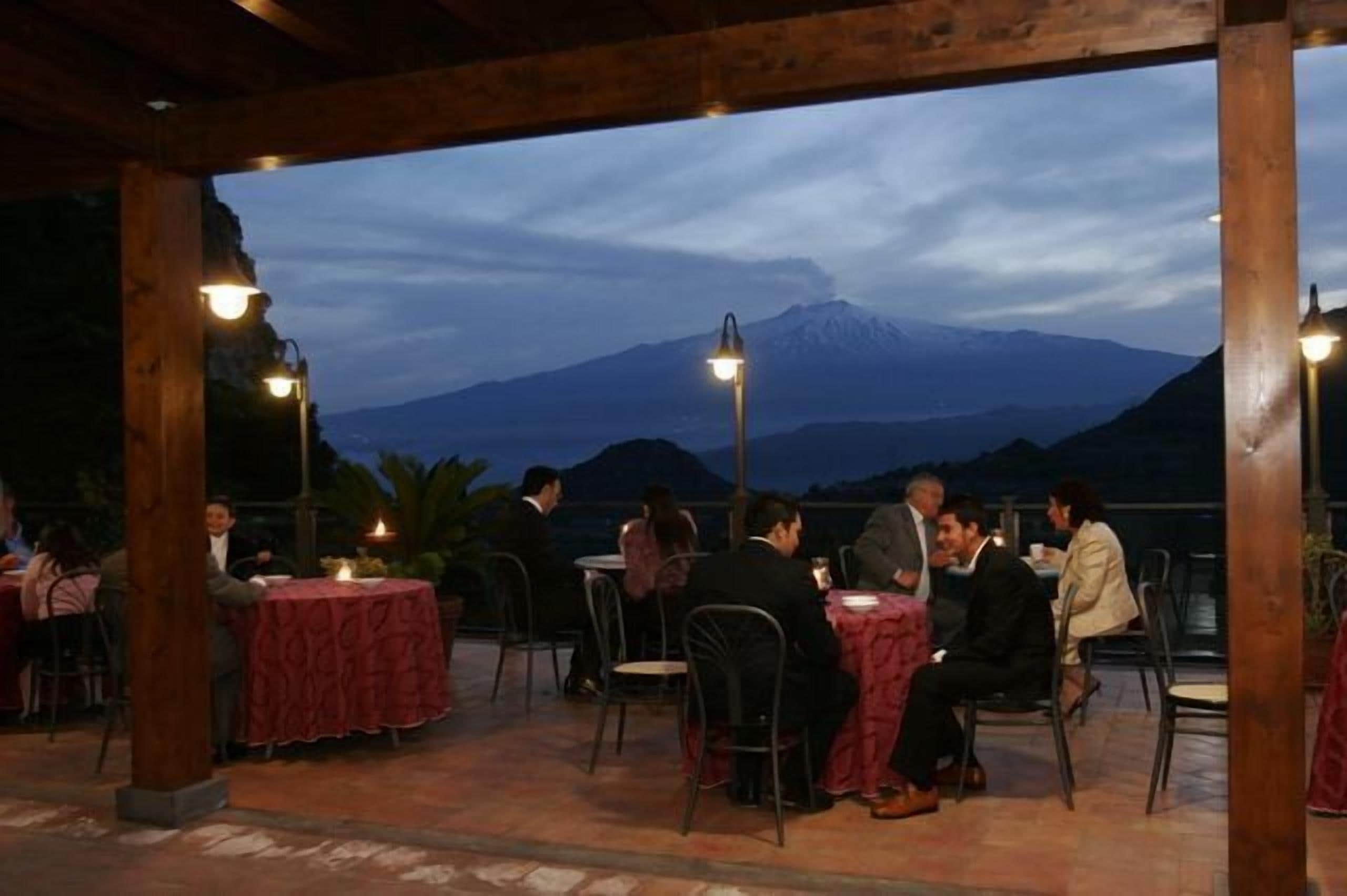 An outdoor dining area with tables and chairs, a mountain view, and wooden beams.