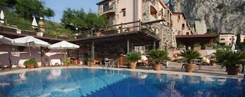 A pool area with a clear blue pool, surrounded by potted plants and outdoor seating.