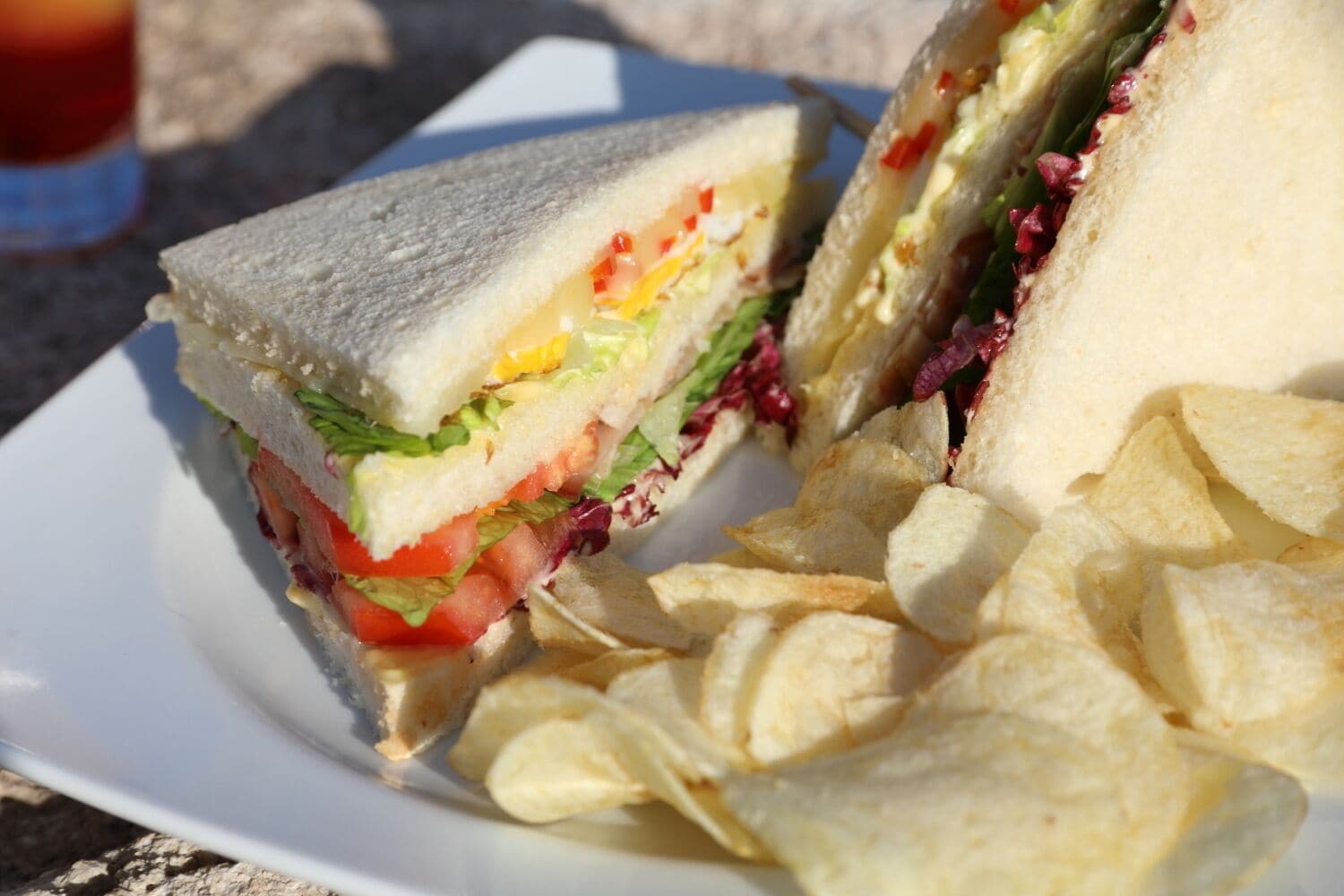 A sandwich cut in half with visible layers of lettuce, tomato, and egg, accompanied by potato chips on a white plate.