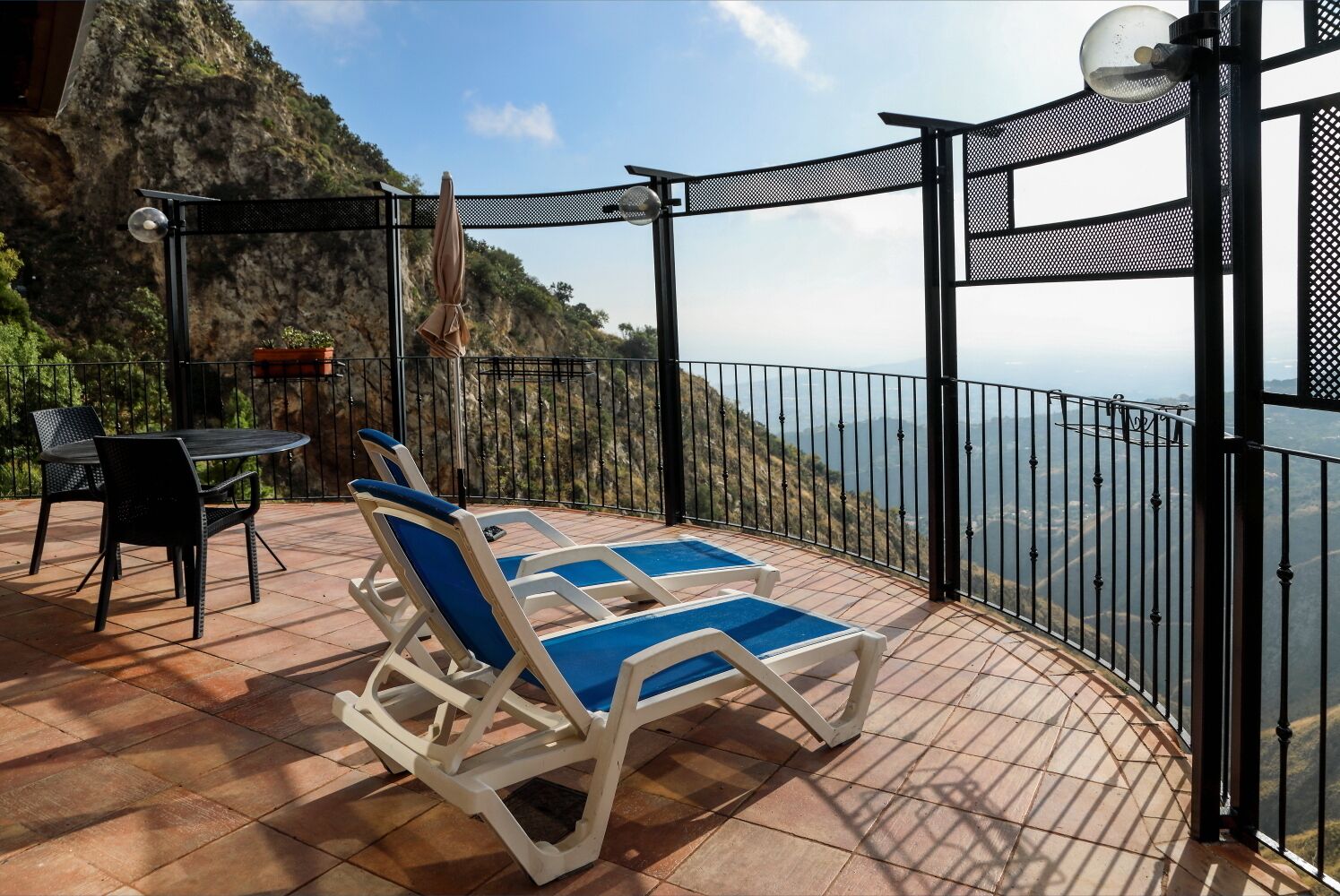 A terrace with two sun loungers and a table, overlooking a mountainous landscape.