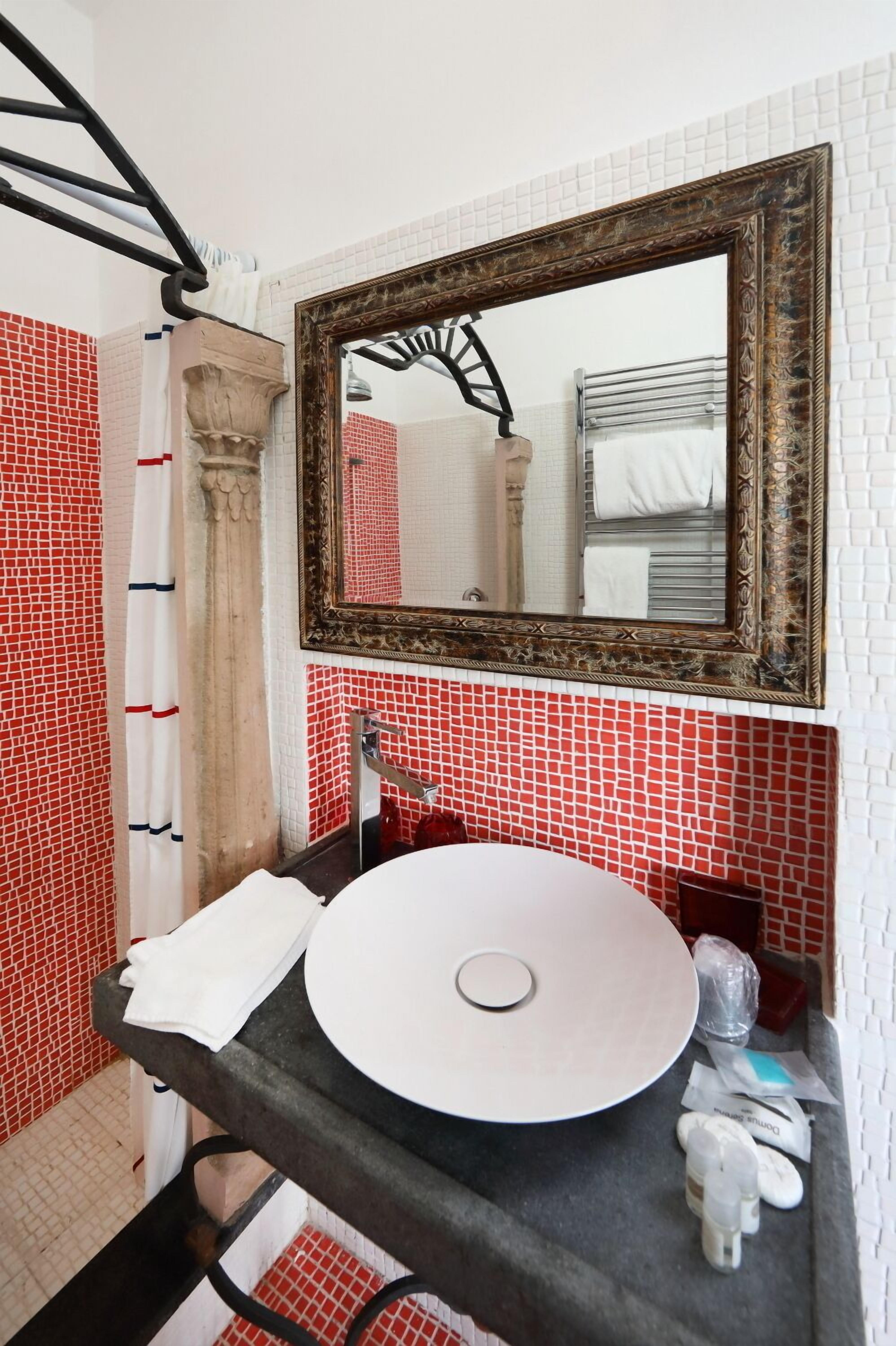 A bathroom with a round sink, a mirror with an ornate frame, and red and white tiled walls.