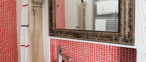 A bathroom with a round sink, a mirror with an ornate frame, and red and white tiled walls.