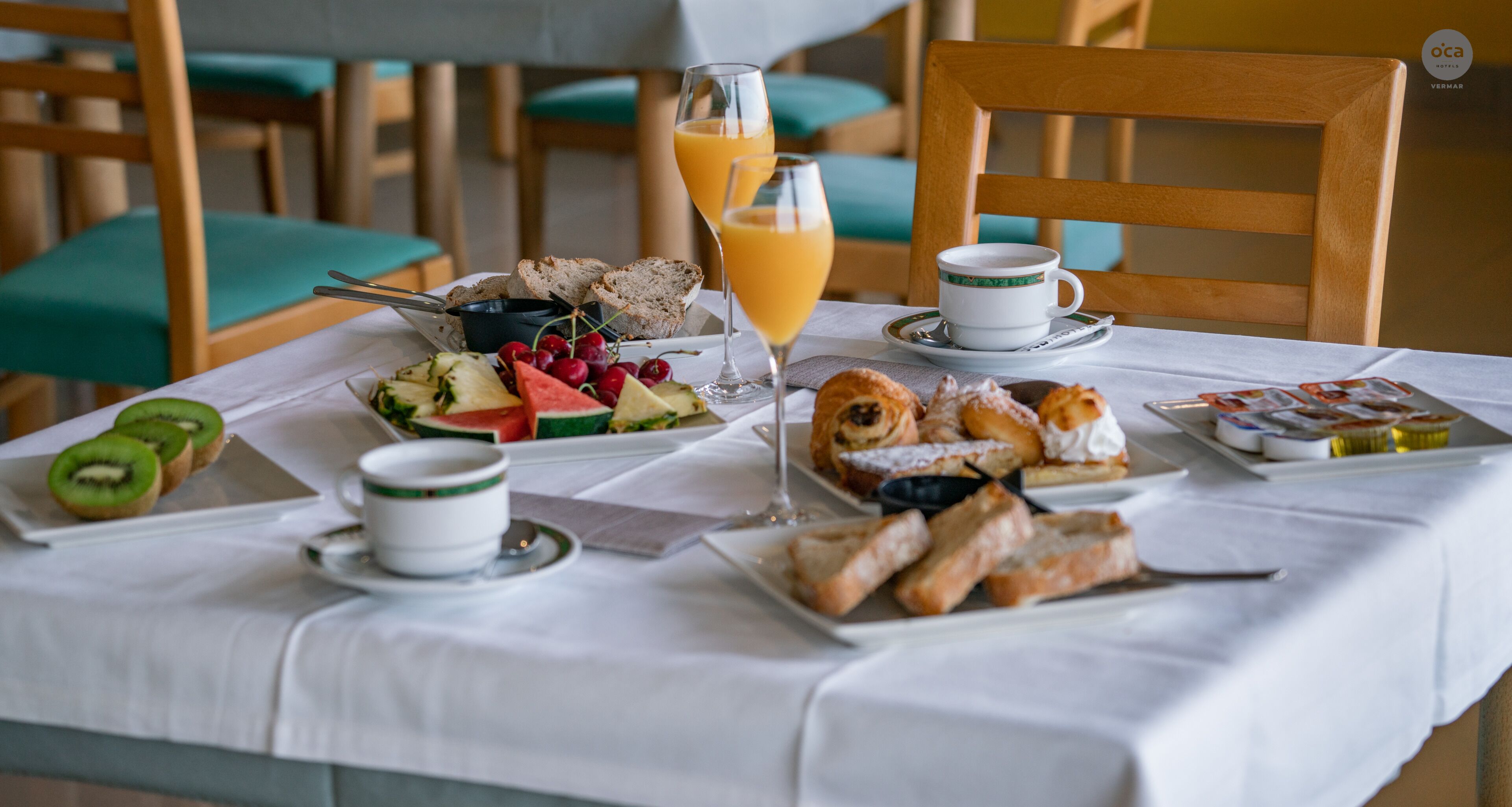 A breakfast setting with a variety of foods, including fruits, pastries, and a glass of orange juice.